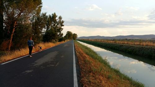 Rear view of man walking on road against sky