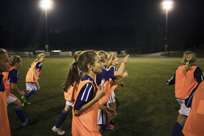 Girls running on illuminated soccer field at night