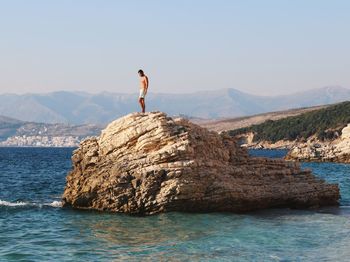 Man standing on rock by sea against sky