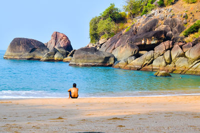 Rear view of shirtless man on rock at beach