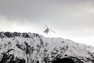 Low angle view of helicopter flying over snowcapped mountain against sky
