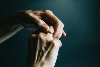 Cropped hand of woman holding wedding ring against colored background