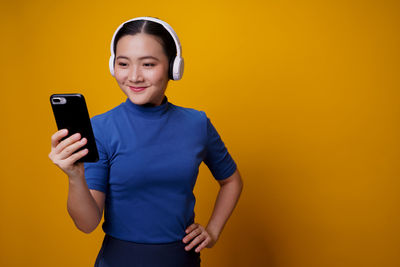 Young man using mobile phone against yellow background