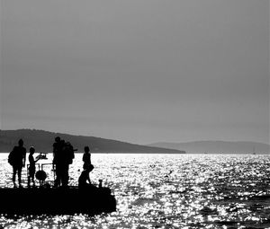 Silhouette men standing on sea against clear sky