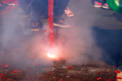 Low section of man standing by burning fireworks on street at night