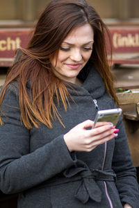 Smiling young woman text messaging on mobile phone