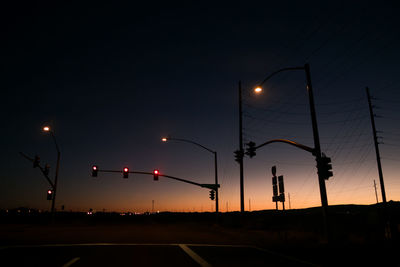 Silhouette stoplights against sky during sunset