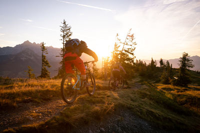 People riding bicycle on mountain against sky during sunset