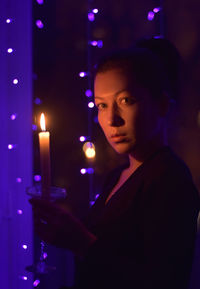 Portrait of woman holding candle while standing at home