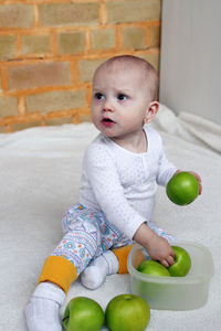 High angle view of cute baby girl sitting on carpet with apple at home