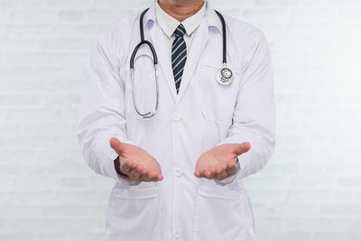 Midsection of doctor gesturing while standing against wall