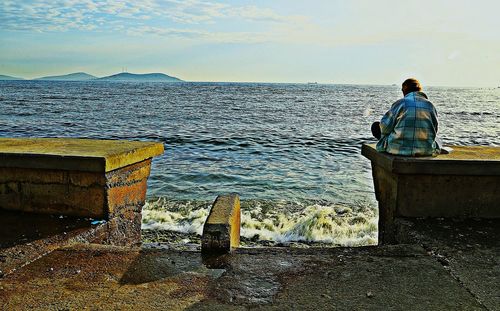 Rear view of man standing by sea against sky