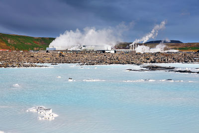 Smoke emitting from industry by sea against sky