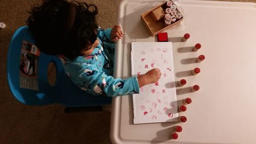 High angle view of little girl painting with stamps on table