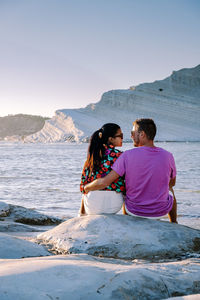 Friends sitting on shore by sea against sky