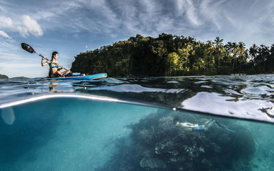 Woman paddleboarding and man snorkeling in sea against sky