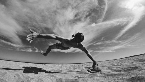 Man backflipping at beach against sky