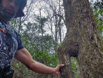 Side view of young man standing by tree trunk in forest