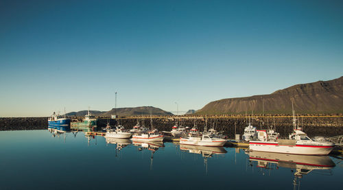 Boats moored in lake against clear blue sky
