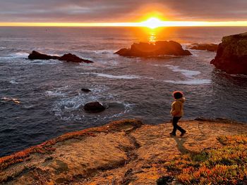 High angle view of woman walking on cliff against sea during sunset