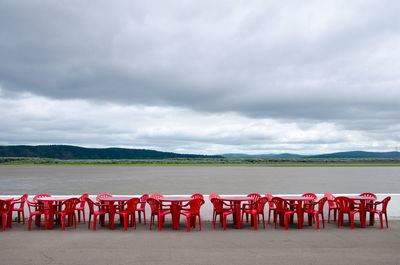 Cafe outdoors. red plastic tables and chairs by the river on a background of hills.