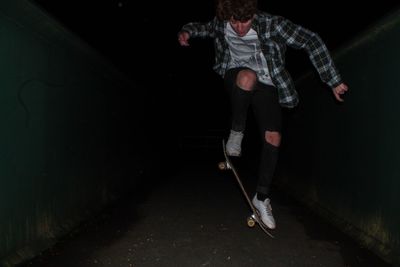 Teenage boy skateboarding on street in dark
