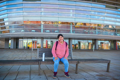 Beautiful woman in casual clothes sits on a wooden bench near the copenhagen opera house. denmark