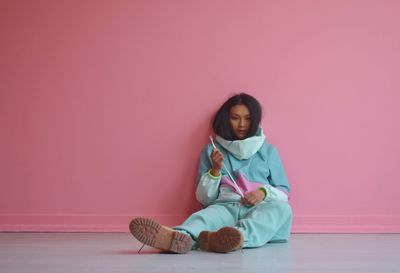 Portrait of woman sitting by pink background