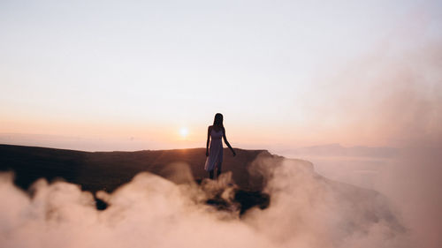 Woman standing on land against sky during sunset