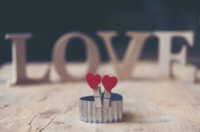 Close-up of heart shape clothespins with text on wooden table against black background