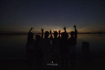 Silhouette people by sea against sky at night
