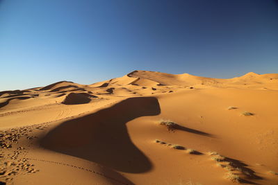 Sand dunes in desert against clear blue sky