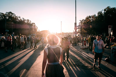 People walking on street in city against sky during sunset