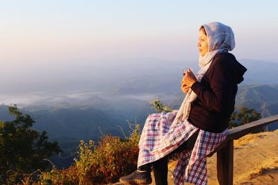 Woman having drink while looking at mountains against sky