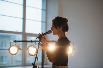 Side view of young woman singing indoors