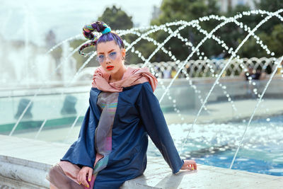 Young funky girl with trendy avant garde fashion style and eyeglasses against fountain