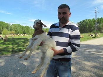 Portrait of man carrying goat on road against sky