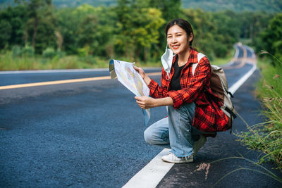 Portrait of smiling young woman holding umbrella on road