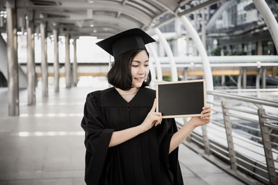Woman wearing graduation gown while standing on bridge