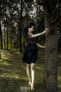 Full length of woman standing by tree trunk in forest