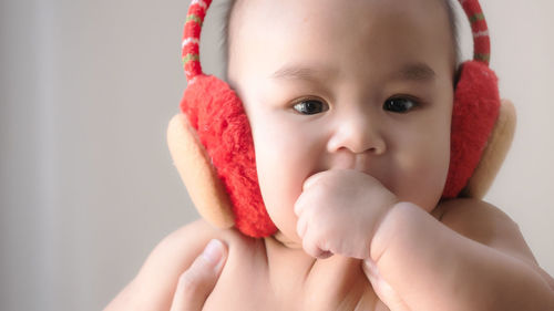 Cropped image of hands holding cute baby boy wearing ear muff against wall