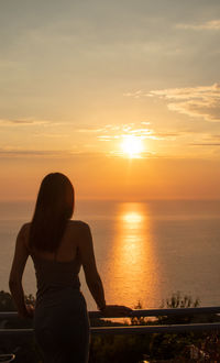 Rear view of woman looking at sea against sunset sky