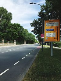 Road sign by trees against sky