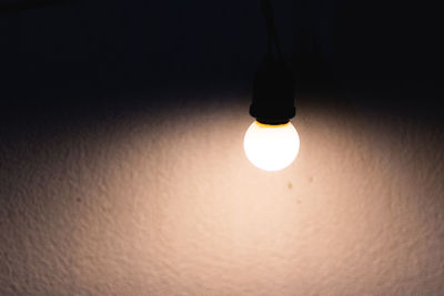 Low angle view of illuminated light bulb hanging on wall