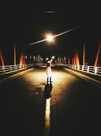 Rear view of woman walking on illuminated road at night