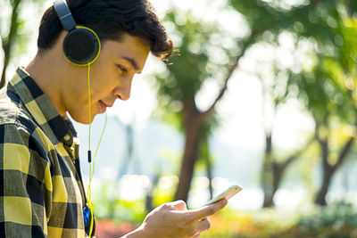 Man listening music while using mobile phone against trees