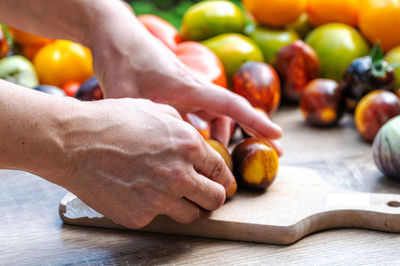 Female hands put tomatoes on a chopping board on the table with different colored tomatoes, closeup