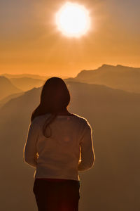 Rear view of woman standing on mountain against sky during sunset