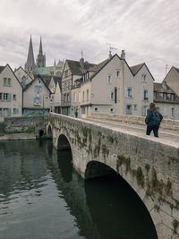 Arch bridge over river by buildings against sky