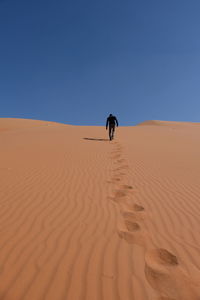 Rear view of man walking on sand dune against clear sky